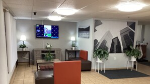A lobby with a seating area, a TV mounted on the wall, and a large wall mural. - Motel 6 Bridgeview, IL (Bridgeview)