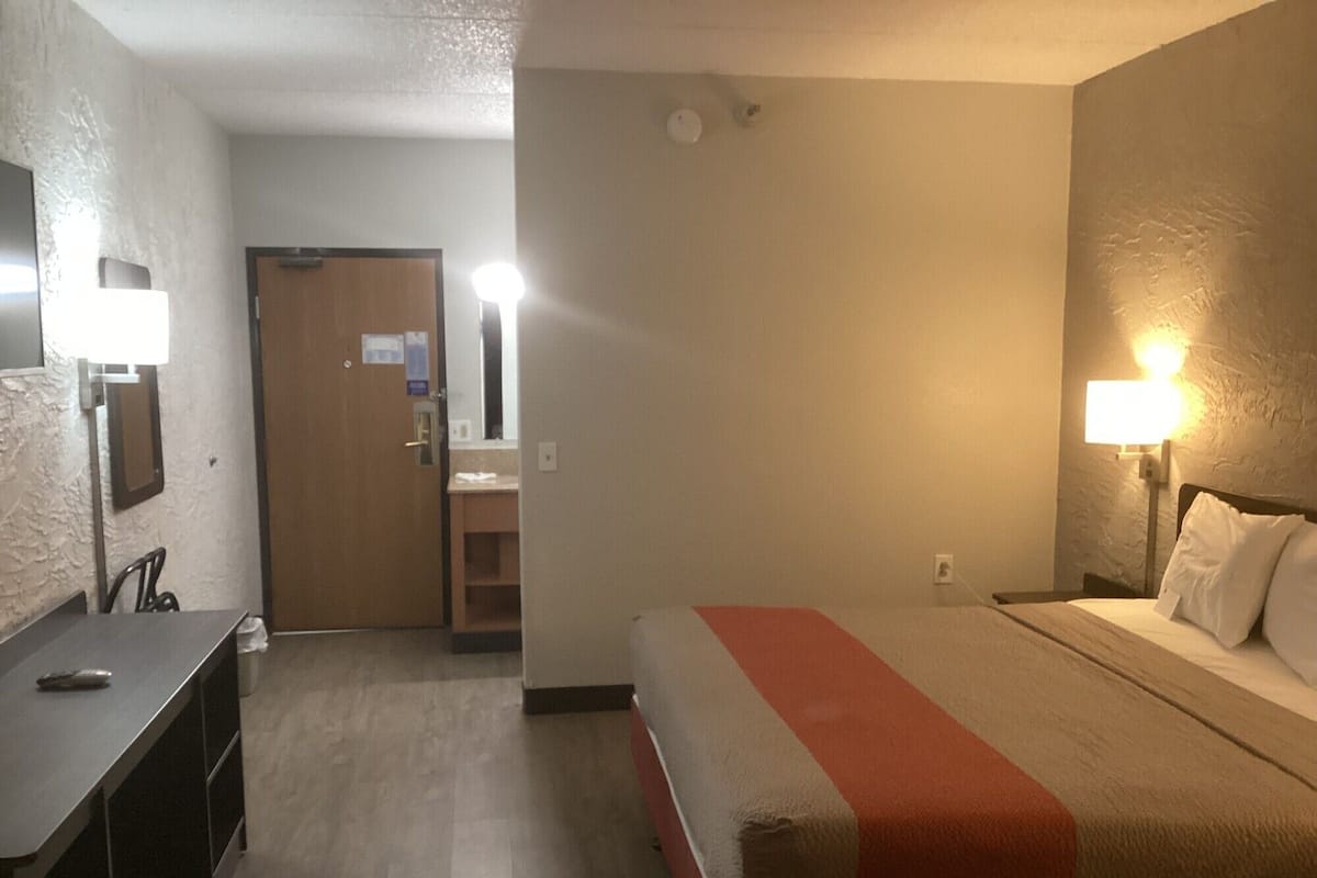 A hotel room with a bed, bedside lamps, a desk, and a mirror.