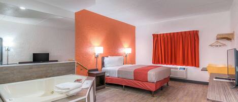 Une chambre d’hôtel avec une grande baignoire, un lit avec une literie rouge, une table de chevet avec une lampe et une fenêtre avec des rideaux rouges.