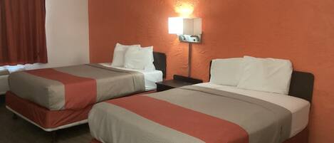 A hotel room with two beds, each with a red and beige bedspread, white pillows, and a nightstand with a lamp.