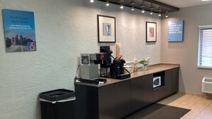 A modern reception area with a coffee machine, trash bin, and framed artwork on the wall. - Motel 6 Bridgeview, IL (Bridgeview)