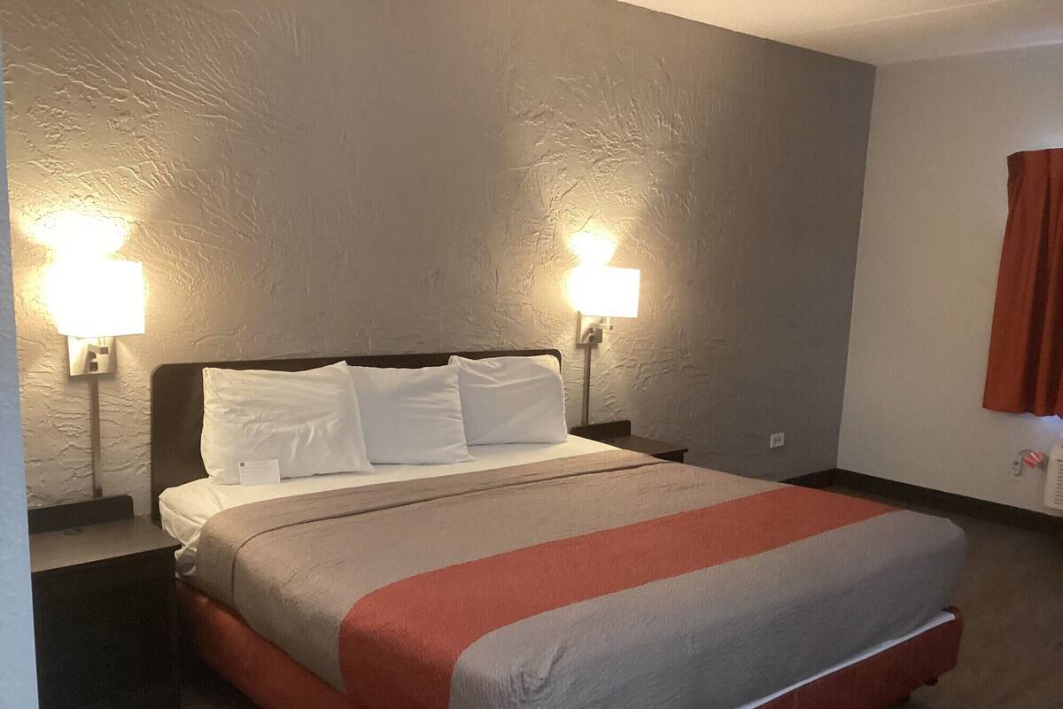 A hotel room with a bed, two bedside lamps, and a red and white striped blanket.