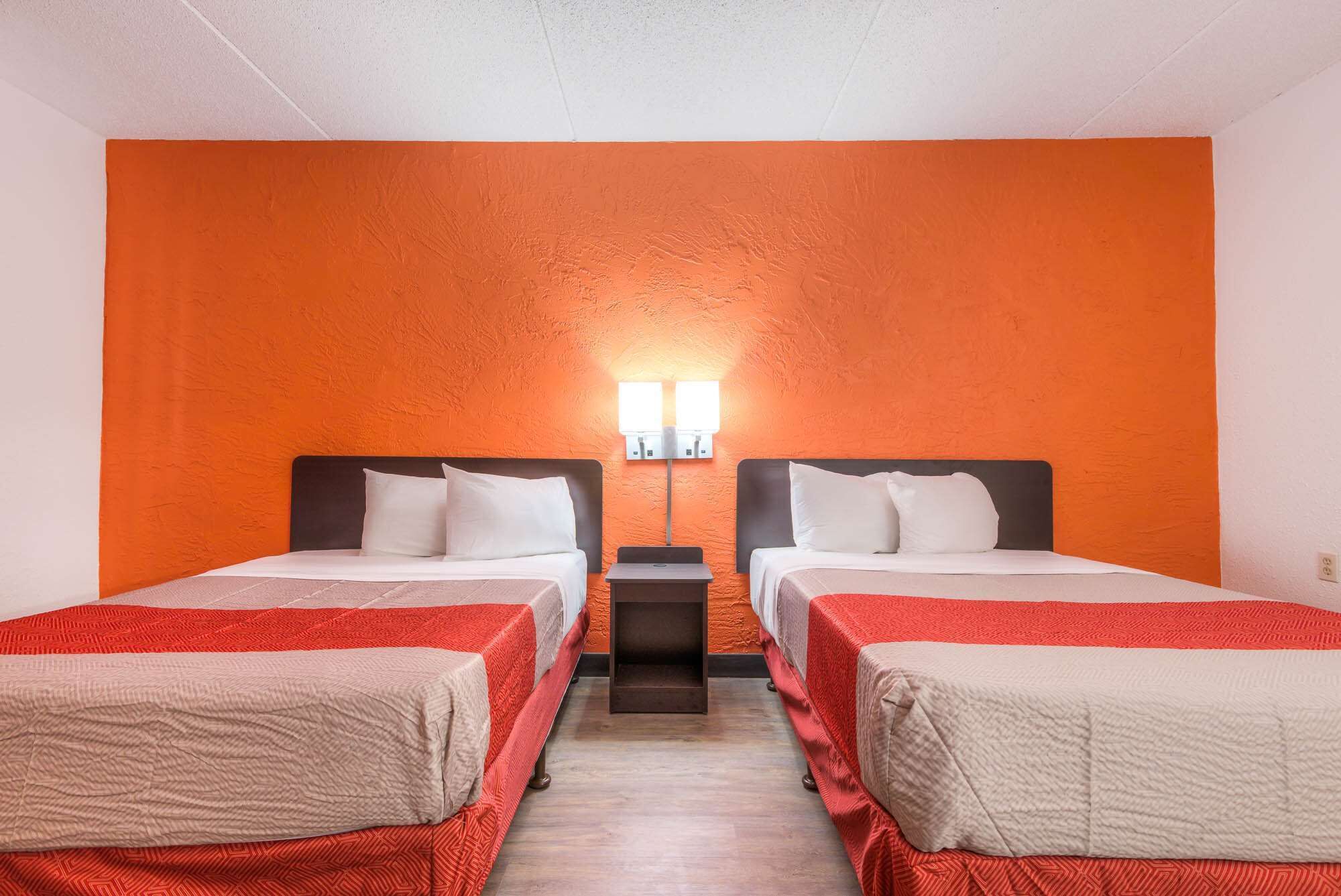 A hotel room with two beds, each with a red and white bedspread, and a large orange wall.