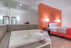 A hotel room with a large bathtub, a bed with red bedding, and a bright orange accent wall. - Motel 6 Bridgeview, IL (Bridgeview)