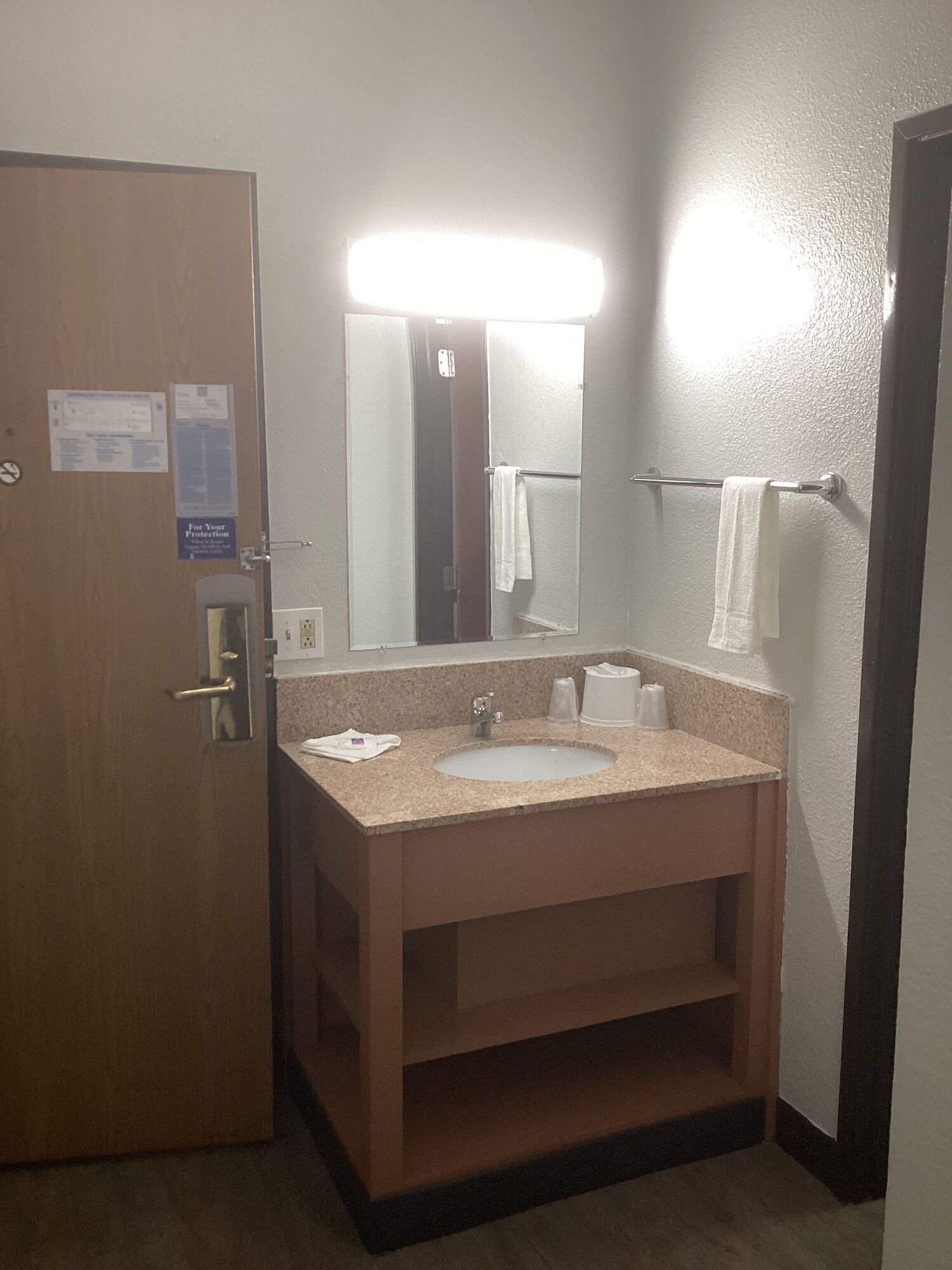 A hotel bathroom with a sink, mirror, towel rack, and a door with a lock.
