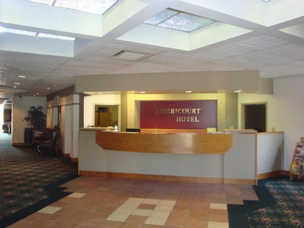 A hotel reception area with a reception desk, a sign reading "AMERICOURT HOTEL," and a patterned carpet.