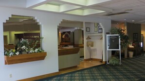 A reception area with a wooden reception desk, a green patterned carpet, and a sign with a welcome message.