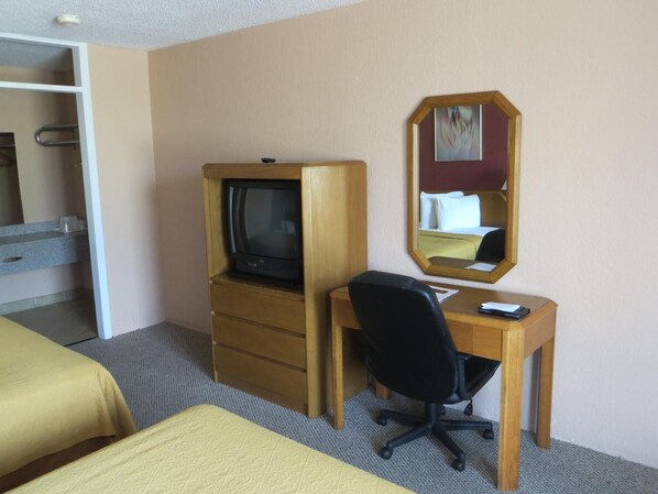 A hotel room with a bed, a desk with a chair, a television, a mirror, and a wardrobe.