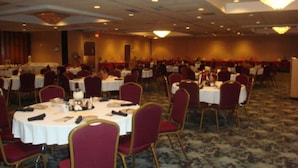 A banquet hall with round tables and chairs, carpeted flooring, and recessed lighting.