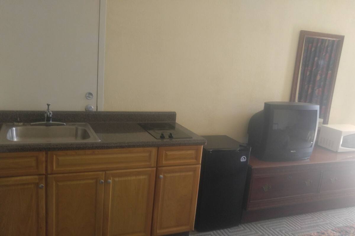 A kitchen with wooden cabinets, a sink, a microwave, and a television on a wooden cabinet.