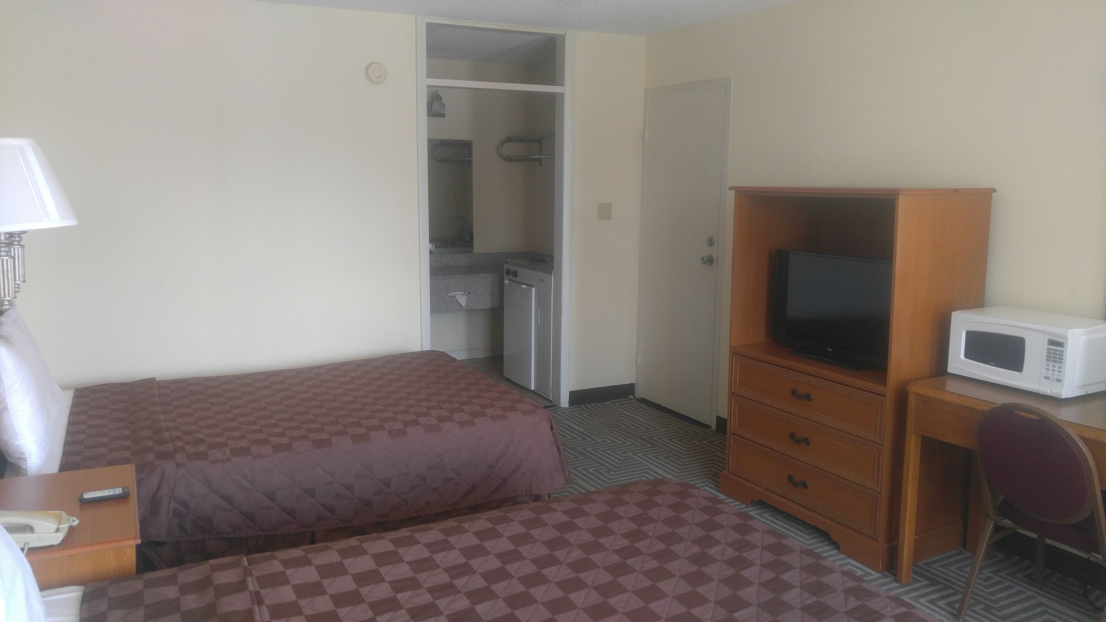 A hotel room with two beds, a desk with a television, a microwave, and a small kitchenette.