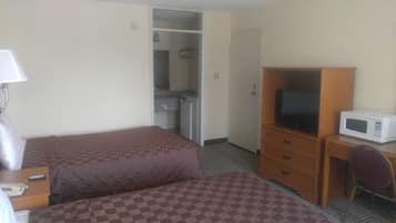 A hotel room with two beds, a desk with a television, a microwave, and a small kitchenette.
