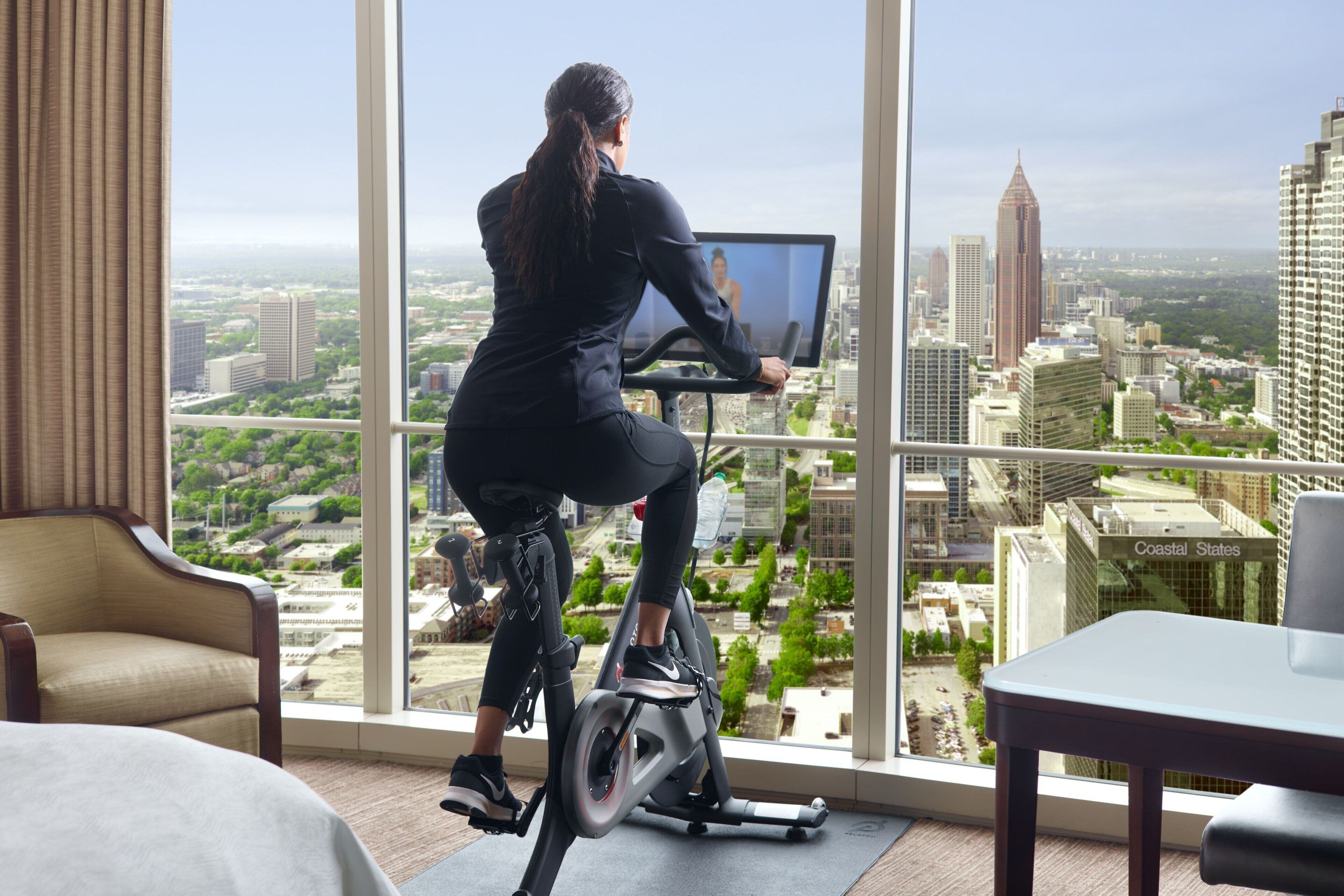 Una persona usando una bicicleta estática con vistas a la ciudad a través de amplias ventanas.