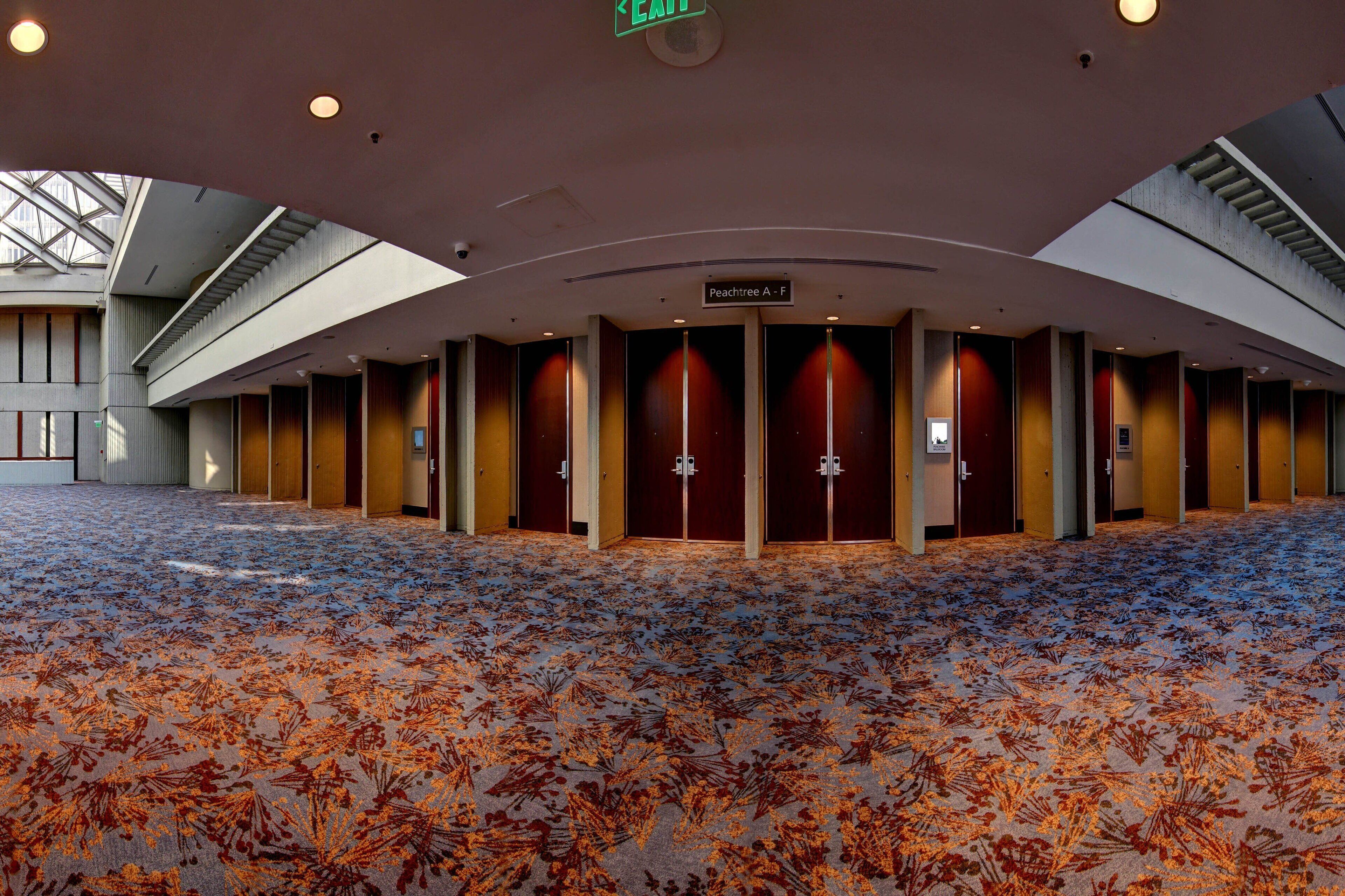 A hotel lobby with a patterned carpet, a sign indicating room Peachtree A - F, and a ceiling with recessed lighting.