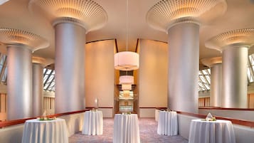 A hotel corridor with high ceilings, large columns, and round tables with white tablecloths.