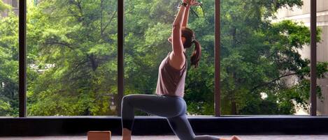 A person performing a yoga pose in a room with large windows overlooking a green park.