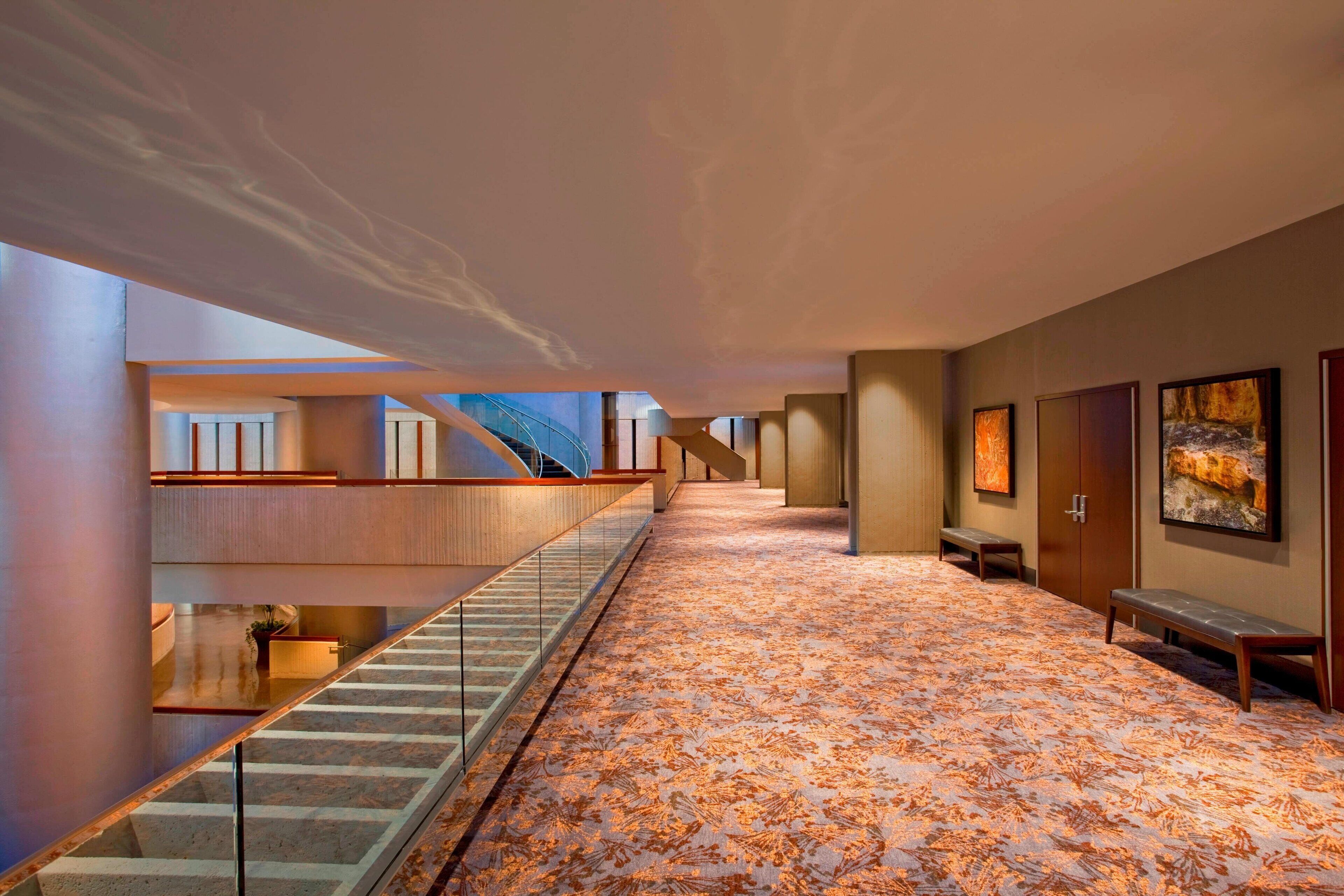 A modern hotel lobby with a patterned carpet, a staircase, and artwork on the walls.