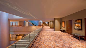 A modern hotel lobby with a patterned carpet, a staircase, and artwork on the walls.