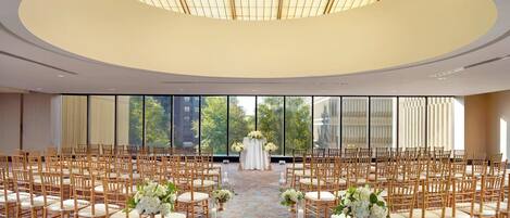 Une grande salle circulaire, dotée d’un plafond haut et d’une allée centrale. La salle est recouverte d’un tapis à motifs et est aménagée avec des rangées de chaises et de tables.