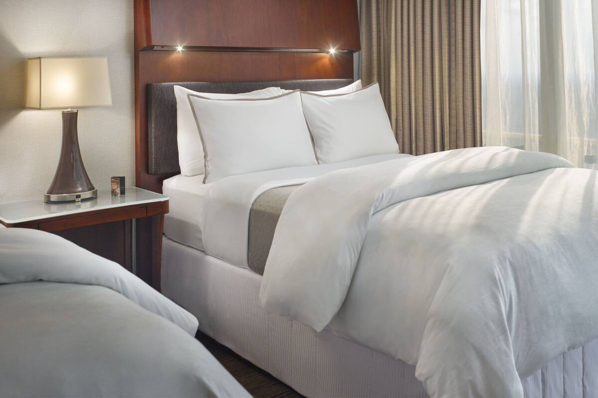 Ein Hotelzimmer mit einem großen Bett, einem Nachttisch mit Lampe und einem Kopfteil mit integrierter Beleuchtung.