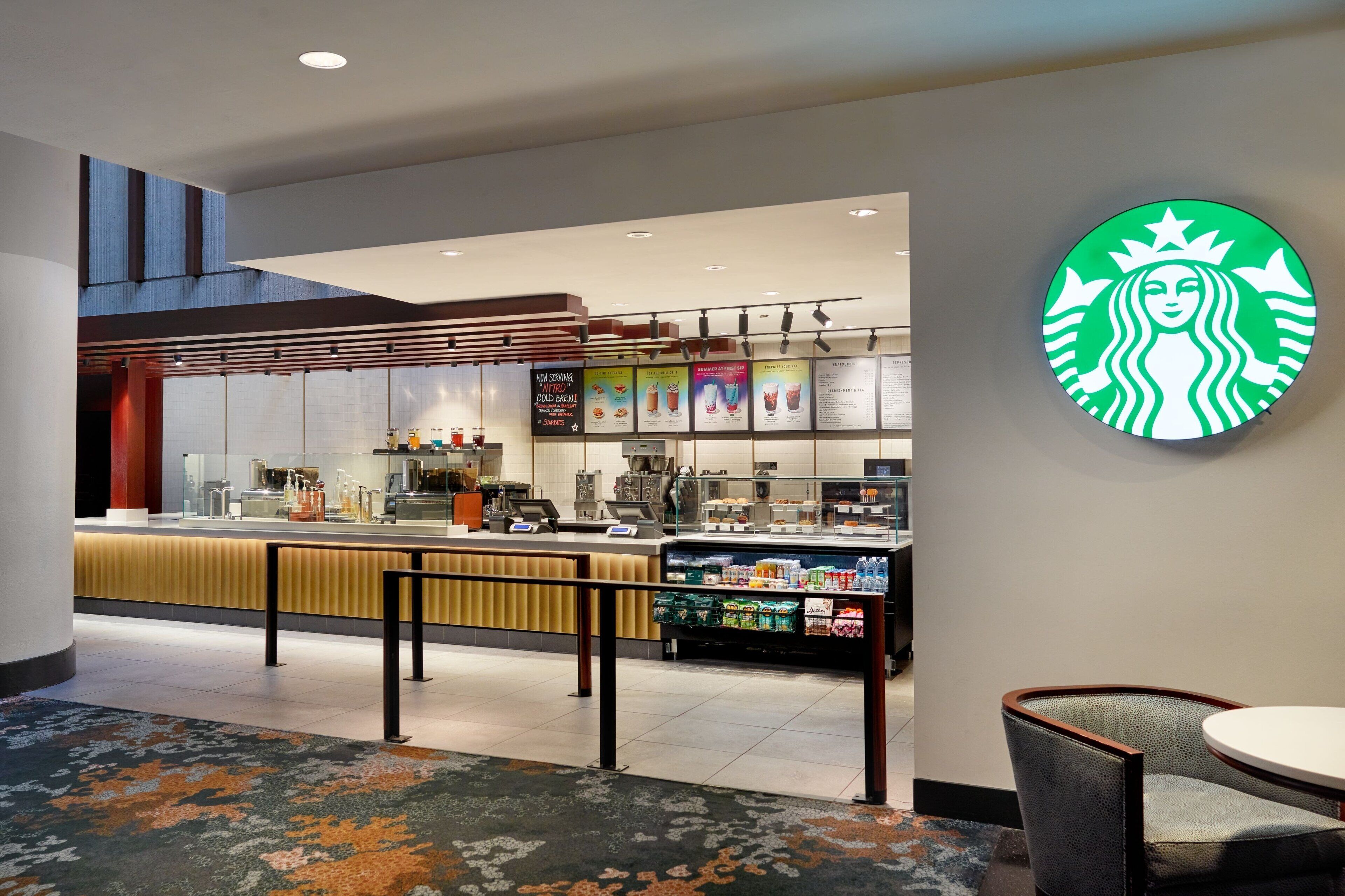 A modern Starbucks with a counter, seating area, and a large illuminated logo on the wall.