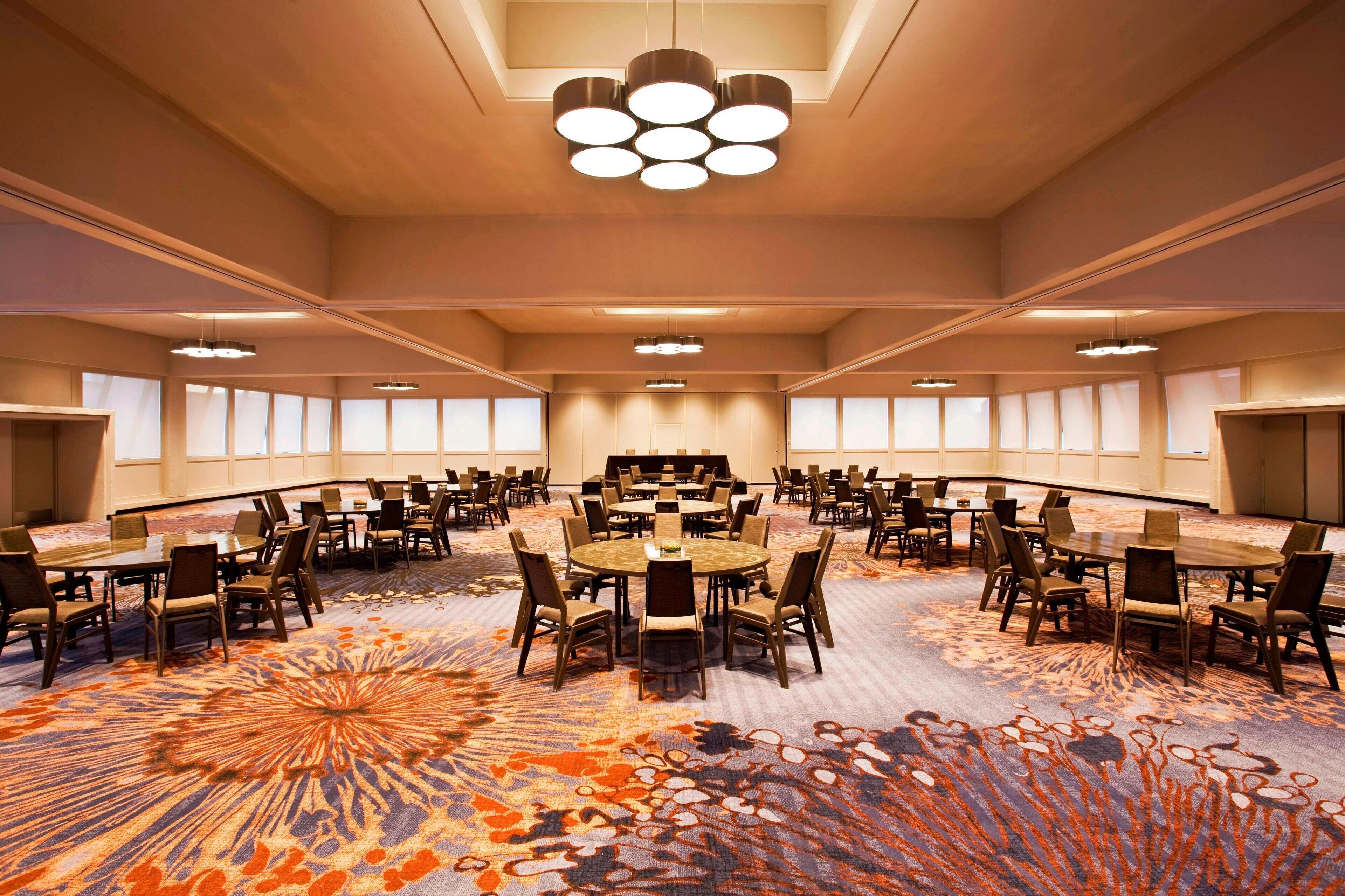 A large conference room with round tables and chairs, a patterned carpet, and a ceiling with multiple light fixtures.
