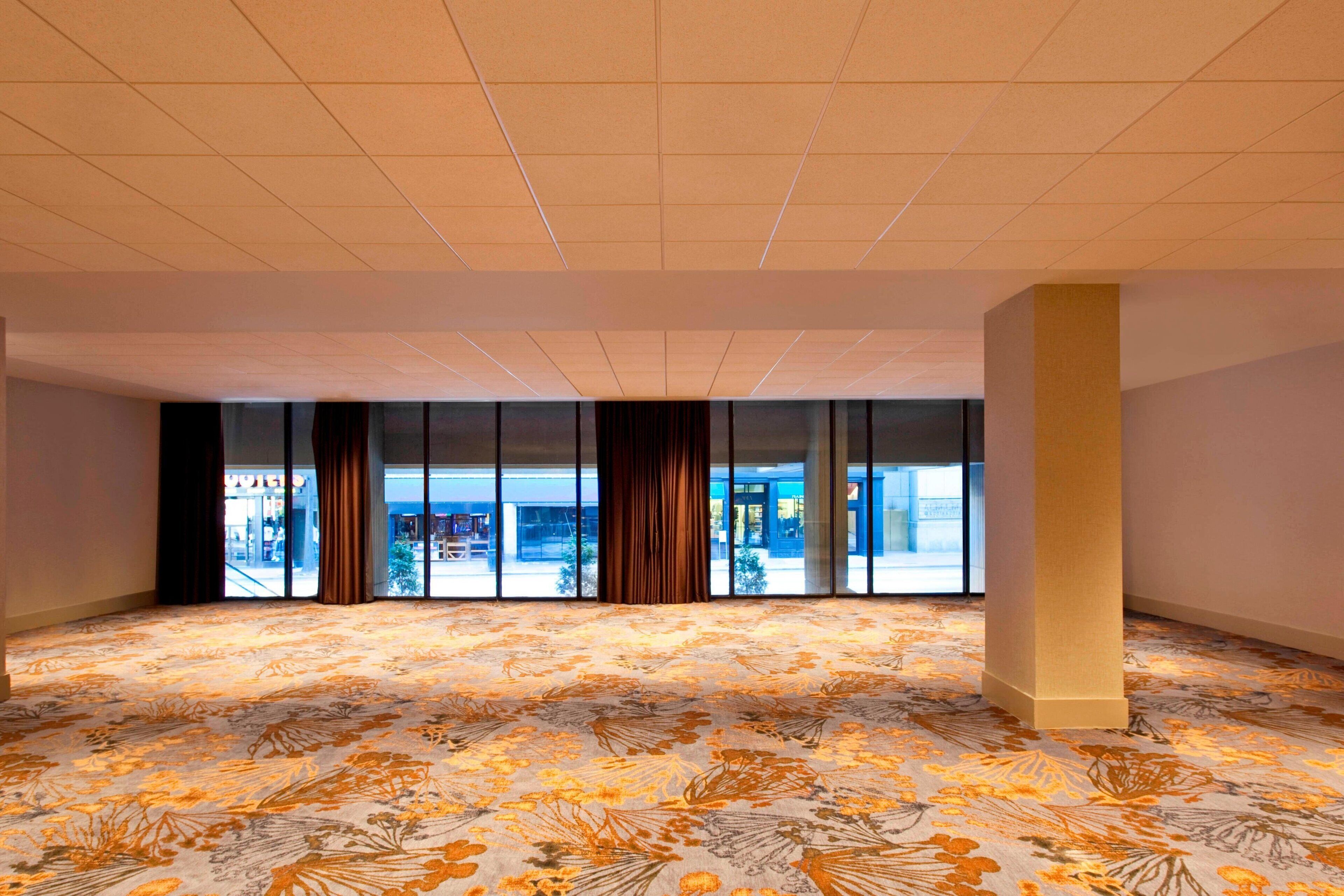 A spacious room with a patterned carpet, large windows, and a pillar.