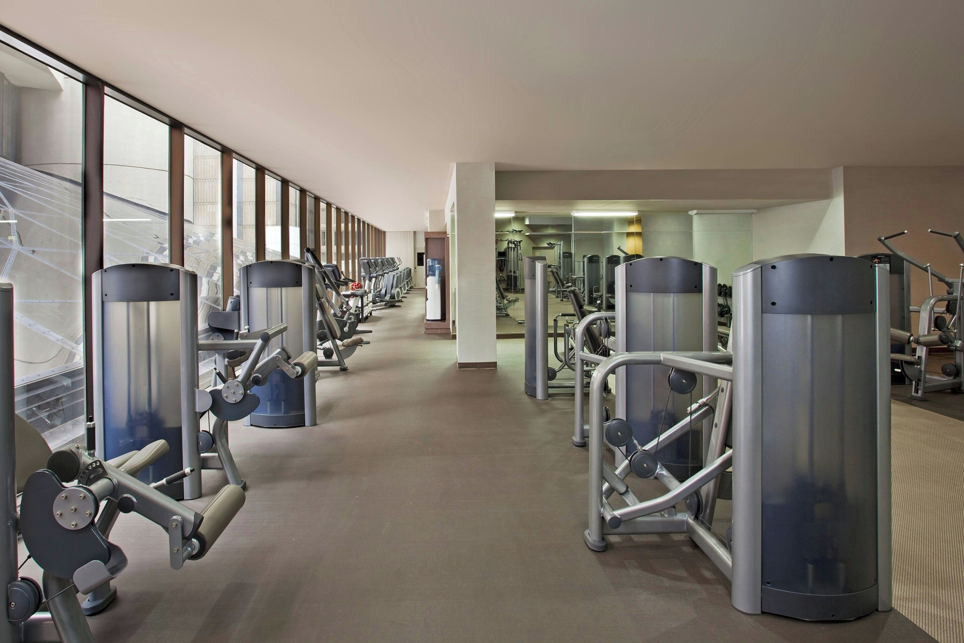 A gym with various exercise machines, a long corridor, and large windows.