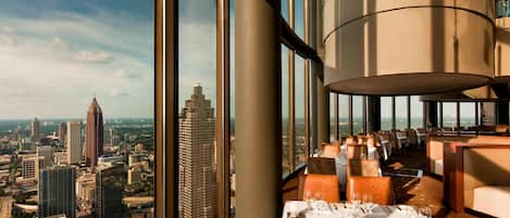 Un restaurant situé dans un immeuble de grande hauteur, offrant une vue sur la ville, doté de grandes fenêtres et d’un aménagement intérieur moderne.
