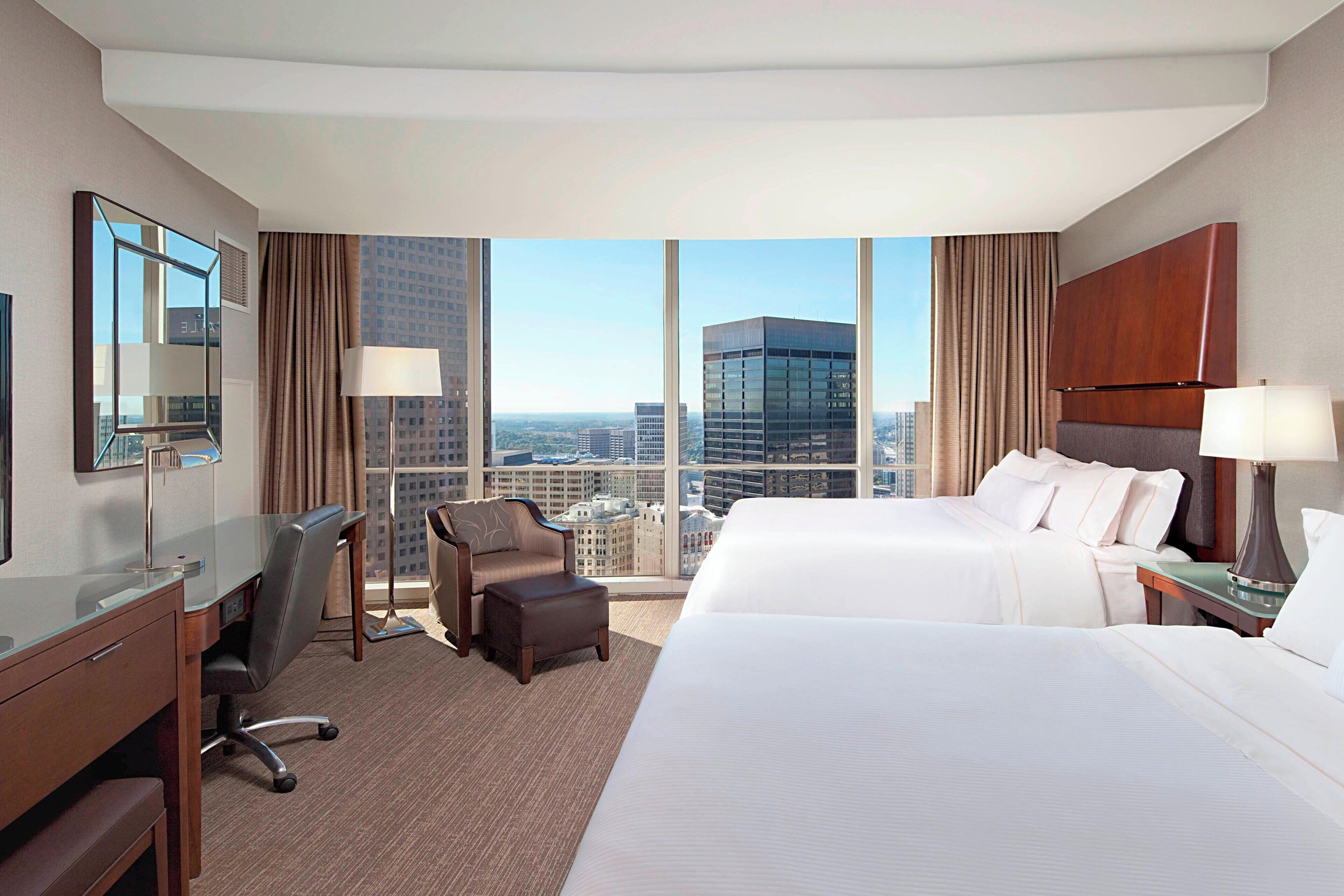 A hotel room with a large bed, a desk, a chair, and a view of the cityscape.