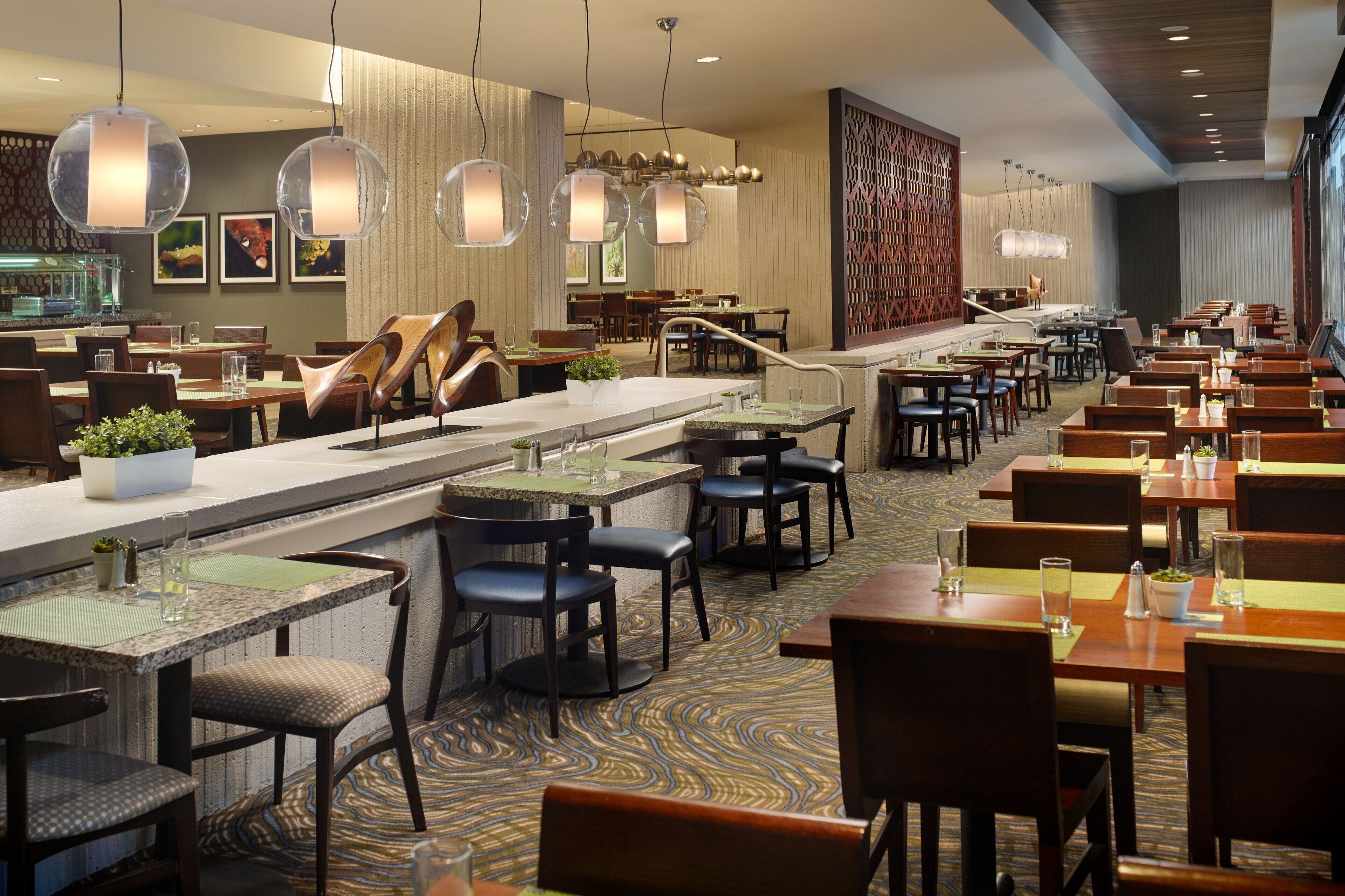 A spacious restaurant with multiple dining areas, a central bar, and modern lighting fixtures.