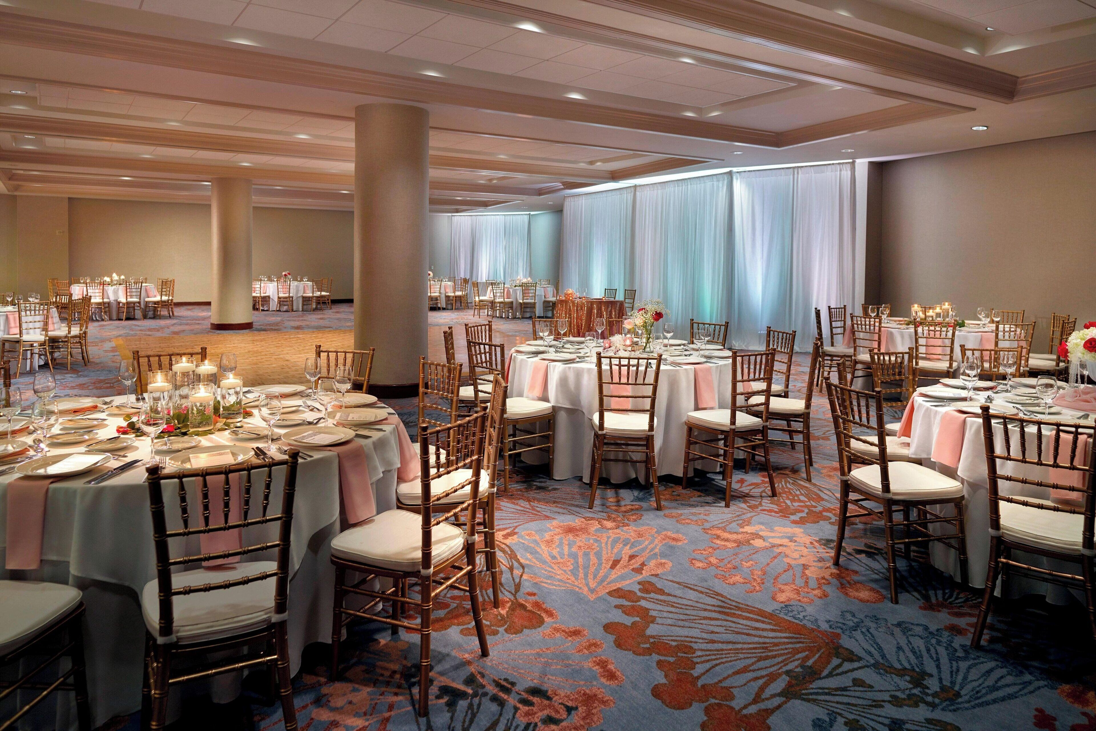 A banquet hall with round tables set for dining, featuring white tablecloths and wooden chairs.