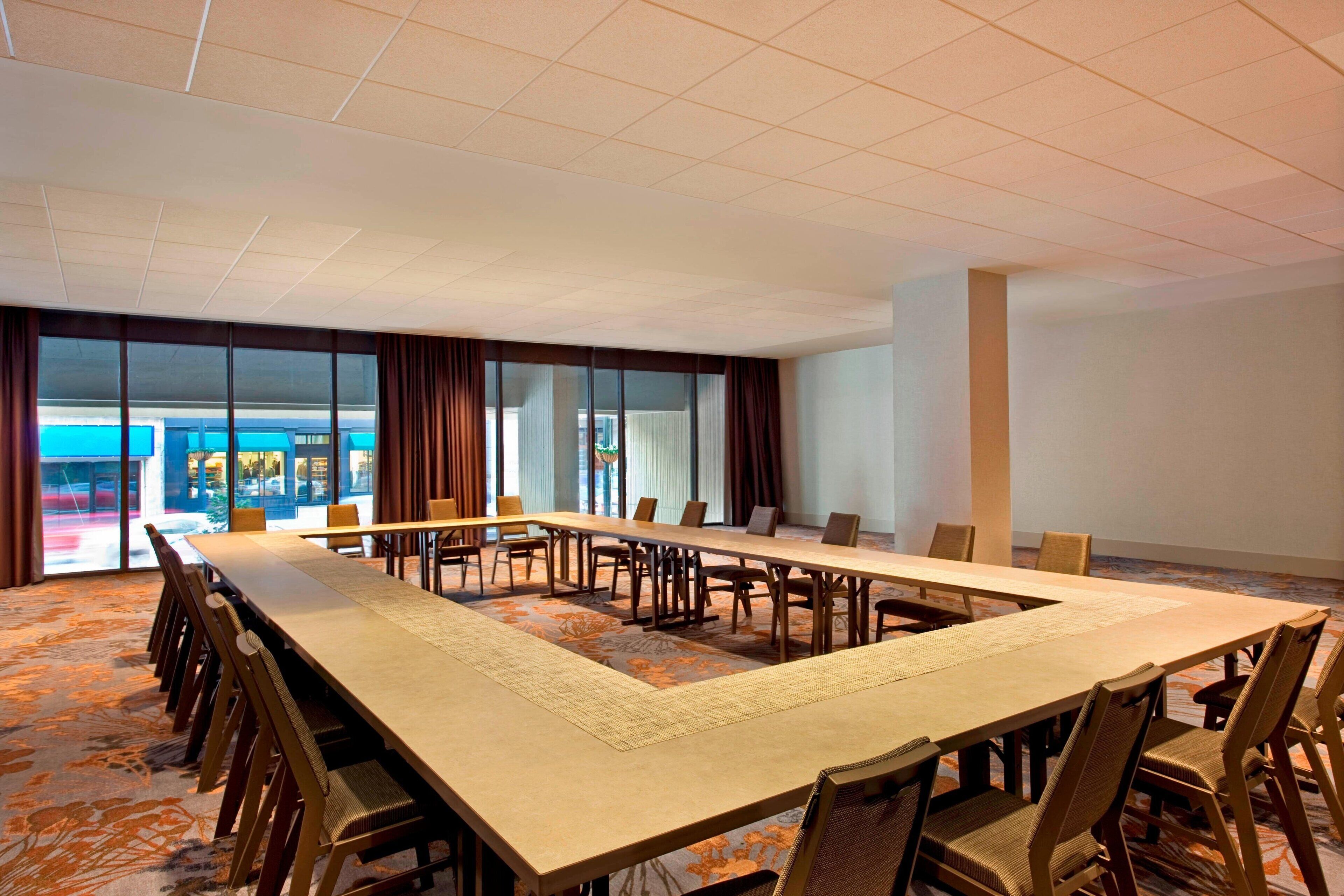 A conference room with a long table, chairs, and large windows with curtains.