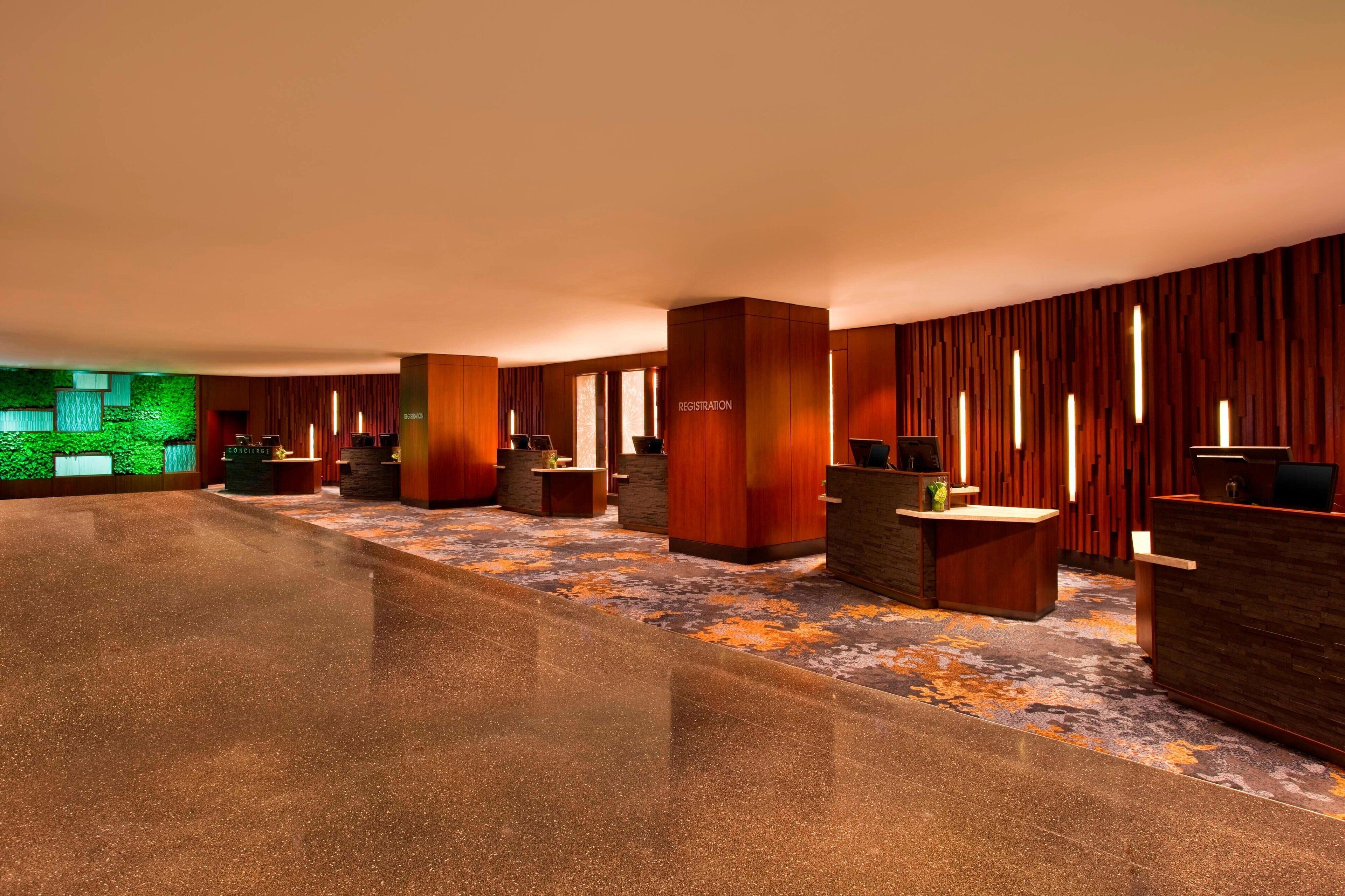 A modern hotel lobby with a polished floor, wooden reception desks, and a green accent wall.