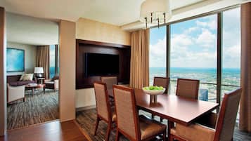 A hotel room with a dining area, a flat-screen TV, and a large window with a city view.