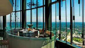 A high-rise restaurant with a panoramic city view, large windows, and a modern chandelier.