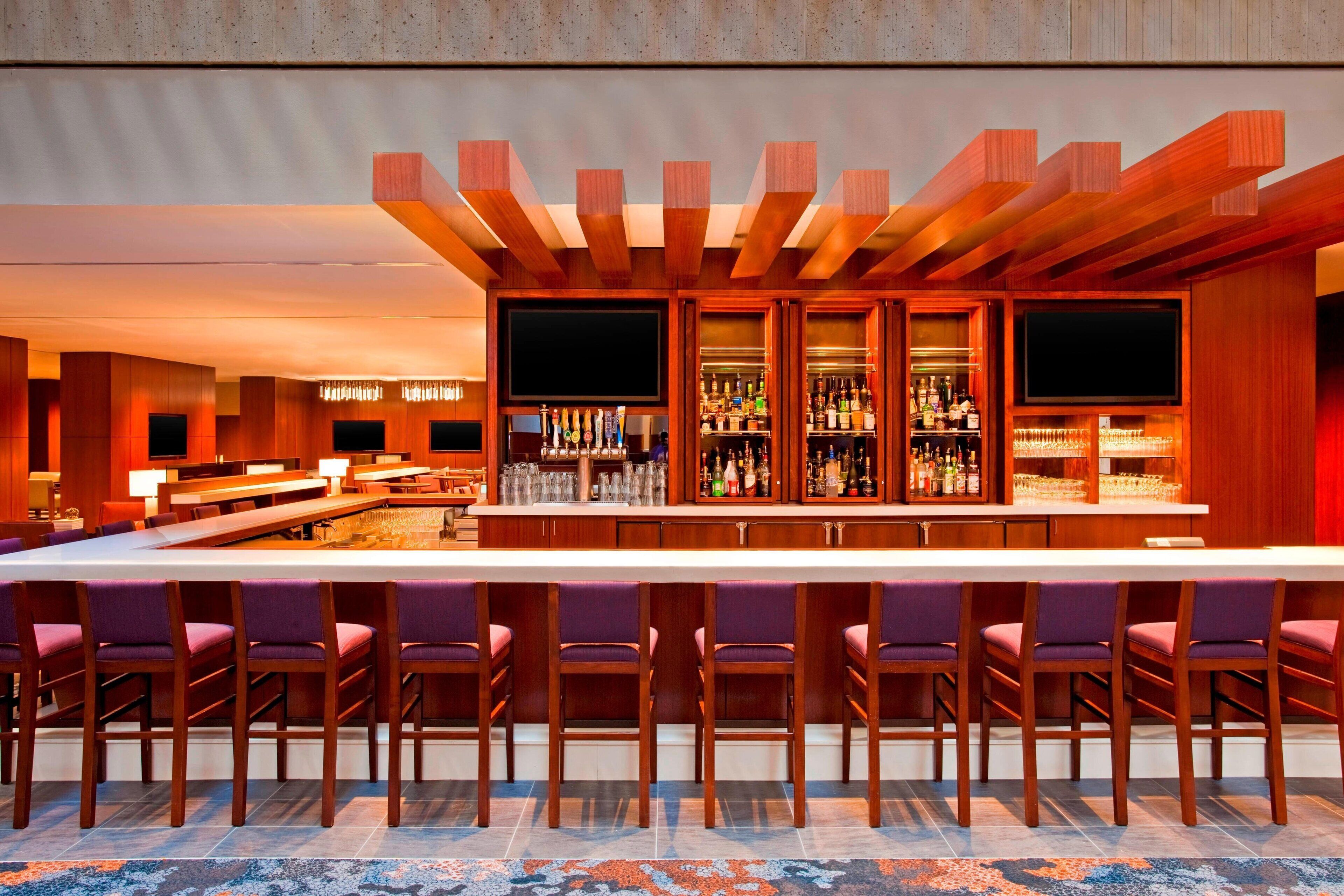 A bar area with wooden bar counters, multiple TVs, and a variety of bottles and glasses.