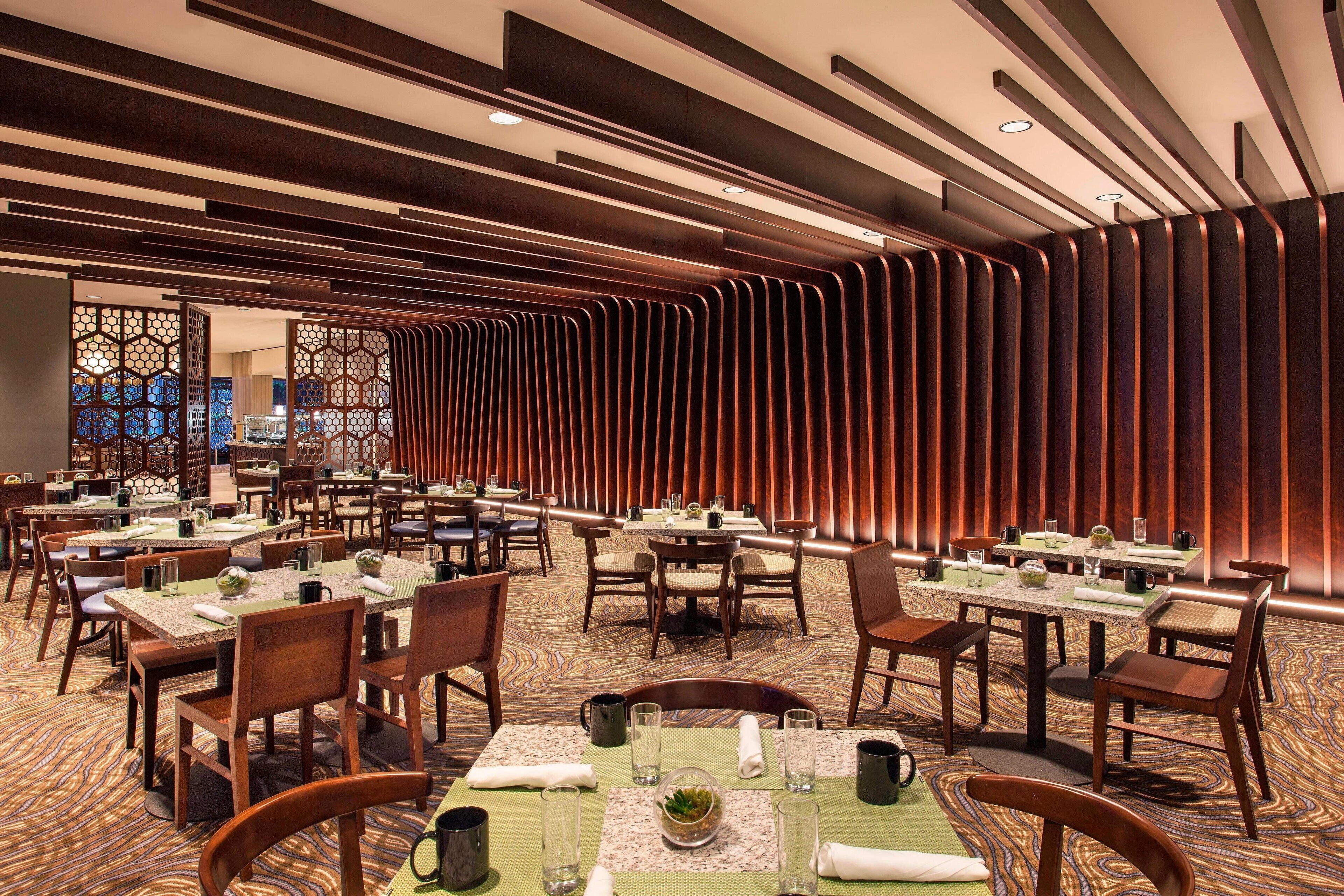 A dining area with multiple tables and chairs, featuring a patterned carpet and wooden paneling on the walls.