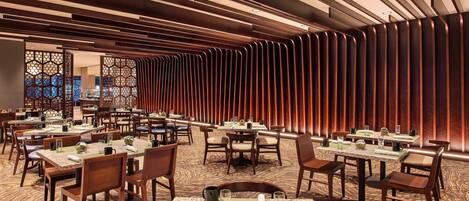 A dining area with multiple tables and chairs, featuring a patterned carpet and wooden paneling on the walls.