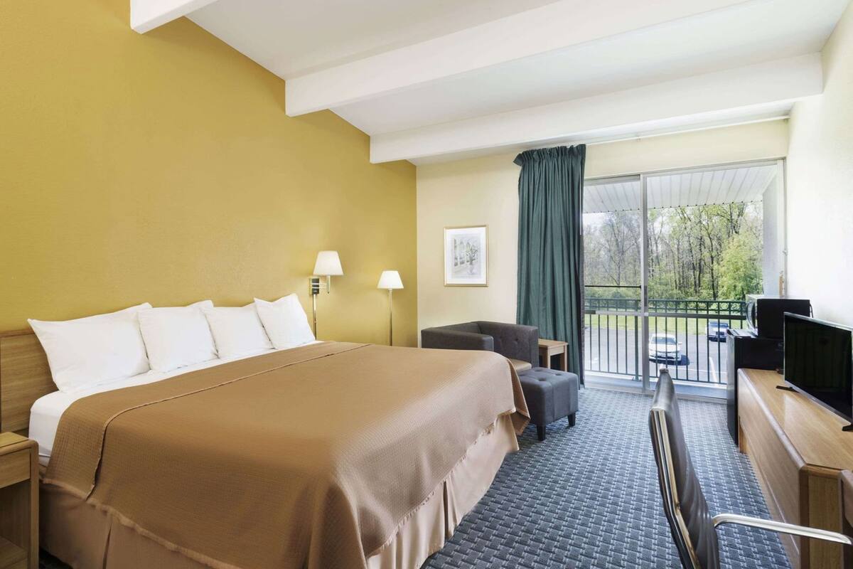 A hotel room with a bed, a desk, a chair, a TV, and a balcony with a view.