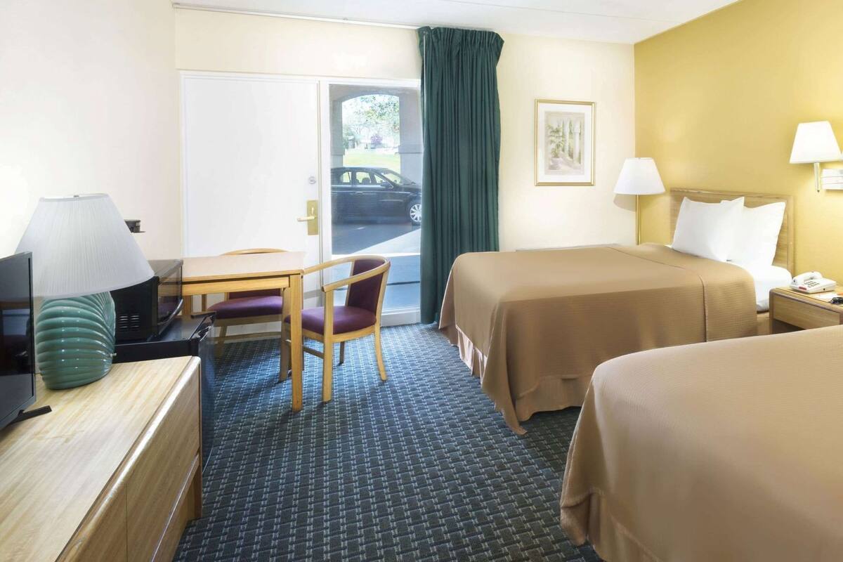 A hotel room with a bed, a desk with a lamp, a chair, and a television.
