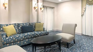 Una habitación con alfombra azul estampada, un sofá azul con cojines, una mesa redonda negra y un sillón beige.
