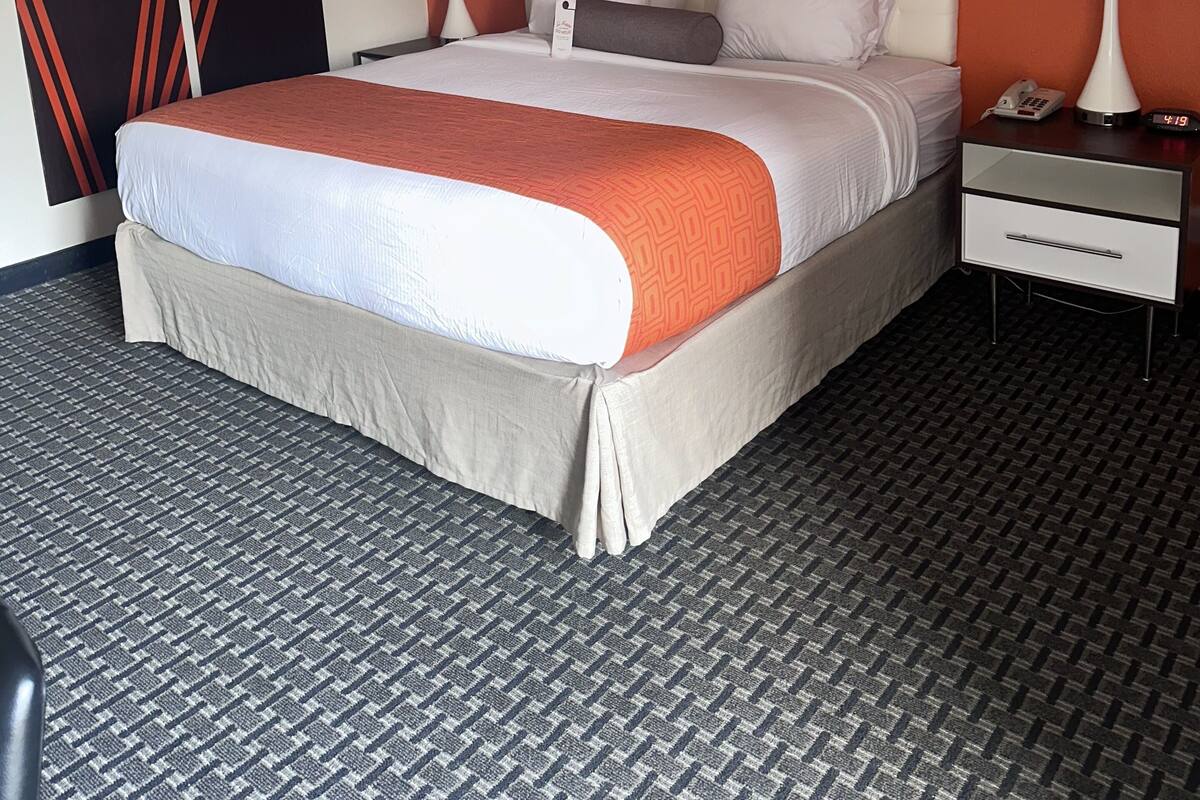A hotel room with a bed, two bedside tables with lamps, a telephone, and a wall with a geometric design.