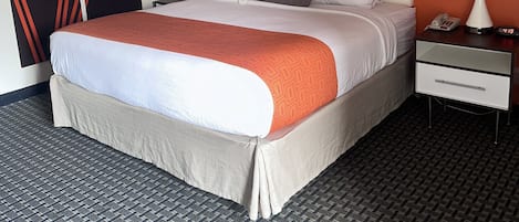Habitación de hotel con cama, dos mesitas de noche con lámparas, teléfono y pared con diseño geométrico.