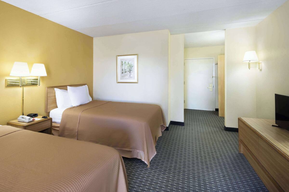 A hotel room with two beds, a desk, a television, and a door leading to another room.