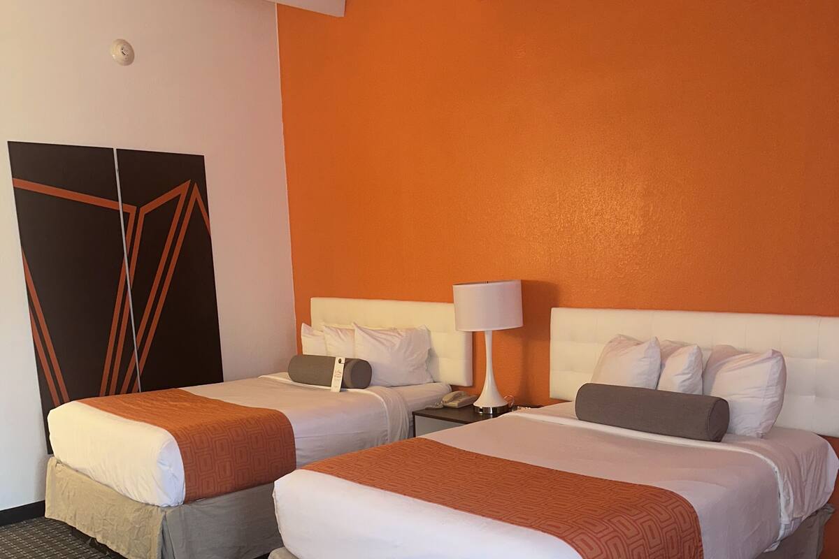 A hotel room with two beds, a large mirror, a nightstand, and a wall clock.
