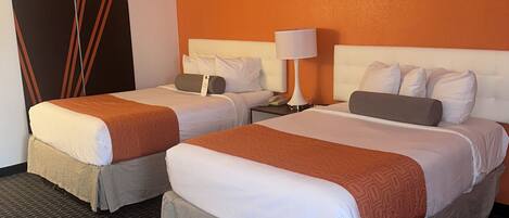 A hotel room with two beds, a large mirror, a nightstand, and a wall clock.
