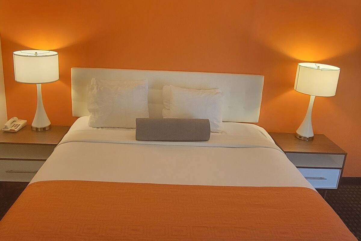 A hotel room with a large bed, two bedside tables, and two lamps.