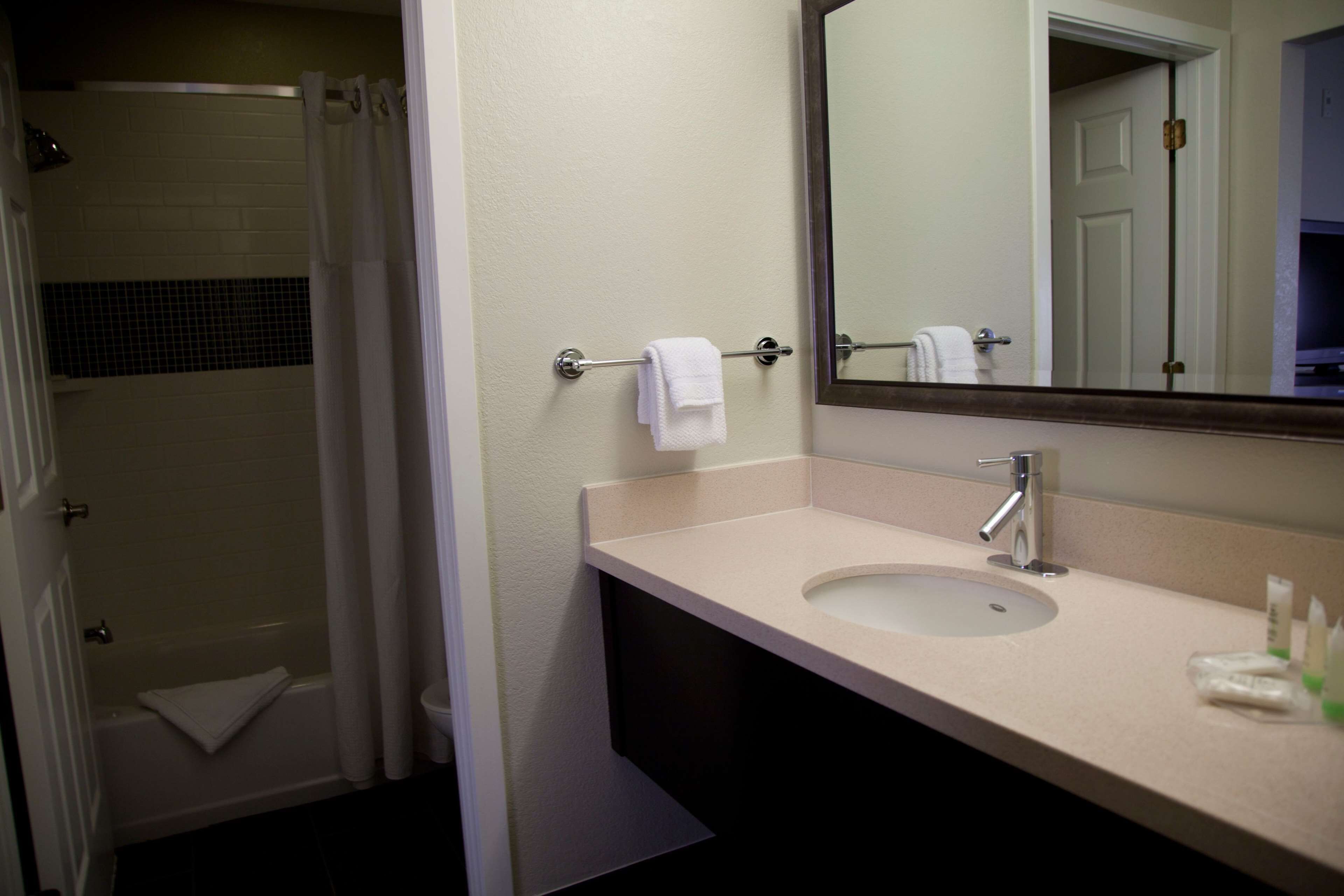 A bathroom with a sink, mirror, towel rack, and shower area.