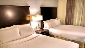 Una habitación de hotel con dos camas, una mesita de noche con lámpara y un cabecero oscuro.